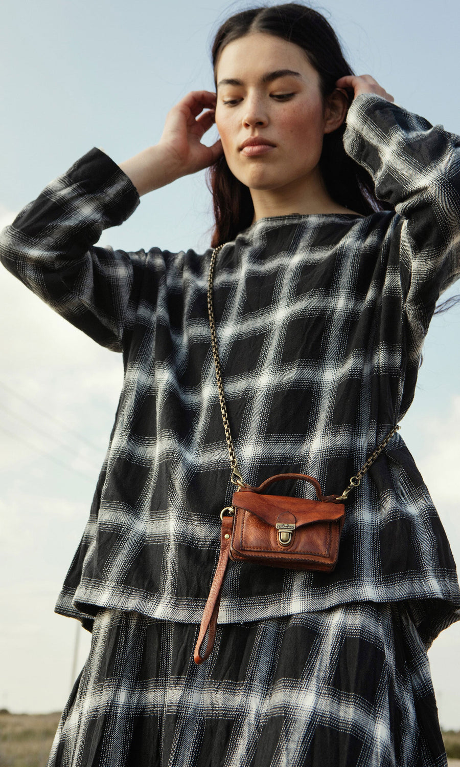 Plümo- Woman in a Gifford Blouse with a small brown crossbody purse, standing outdoors.