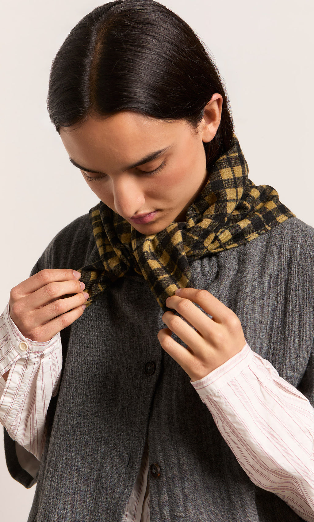 Plümo  Person looking down, tying a Quadrant Necktie over a gray buttoned vest and striped shirt.
