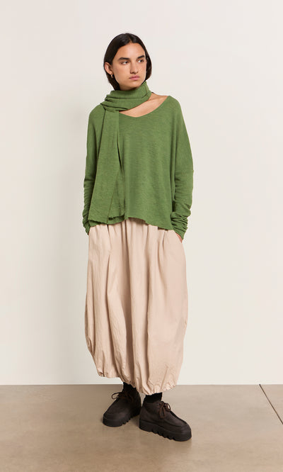 Plümo  Person in a green top, matching scarf, Edina Skirt - Nougat, and black shoes stands against a plain light background.