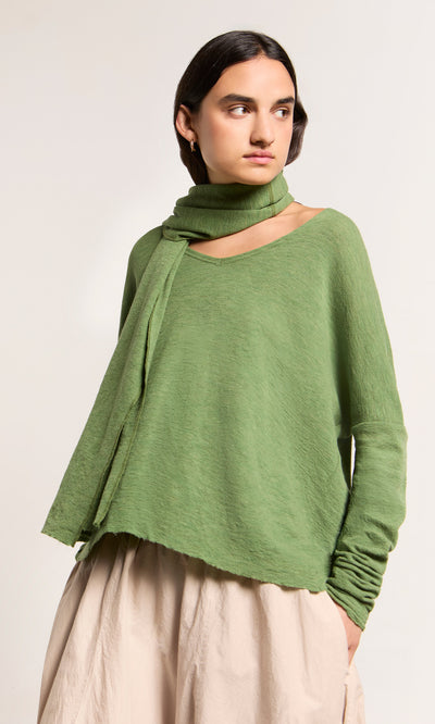 Plümo  Woman in green top and beige skirt wears the Renee Scarf, looking left against a plain background.