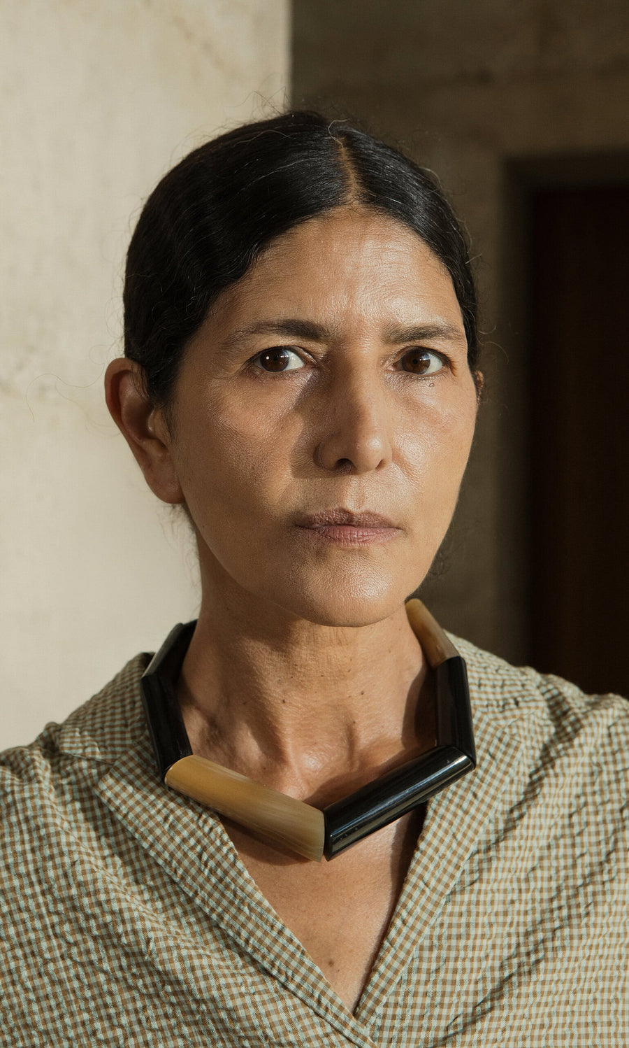 Plümo- A woman with dark hair in a checked shirt wears the chunky handmade Rhia Necklace, looking seriously at the camera.