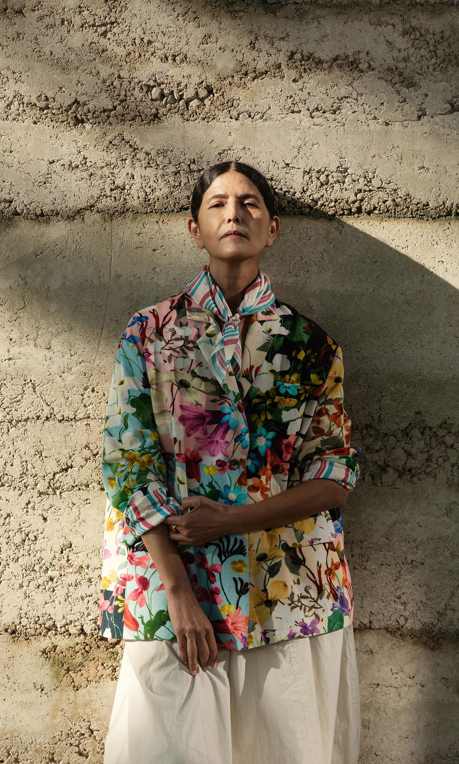 Plümo- Model wears the Riverene Blazer and white pants, standing against a textured concrete wall in natural light.