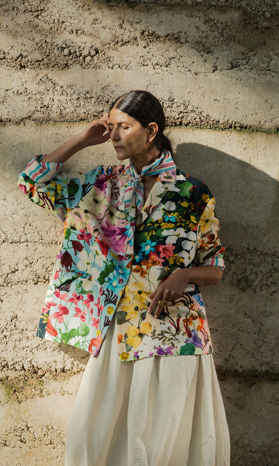 Plümo- Woman wearing the Riverene Blazer stands against a textured wall, eyes closed, hand gently touching her head.