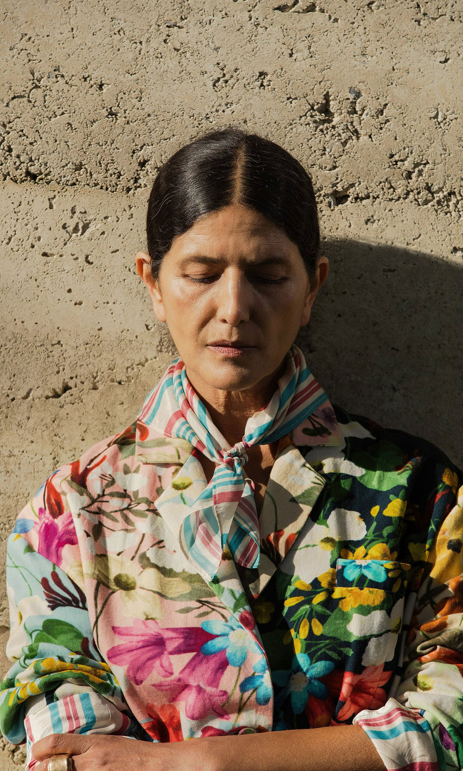 Plümo- Person with dark hair and eyes closed wears a Rimini Stripe Necktie, standing against a textured wall.