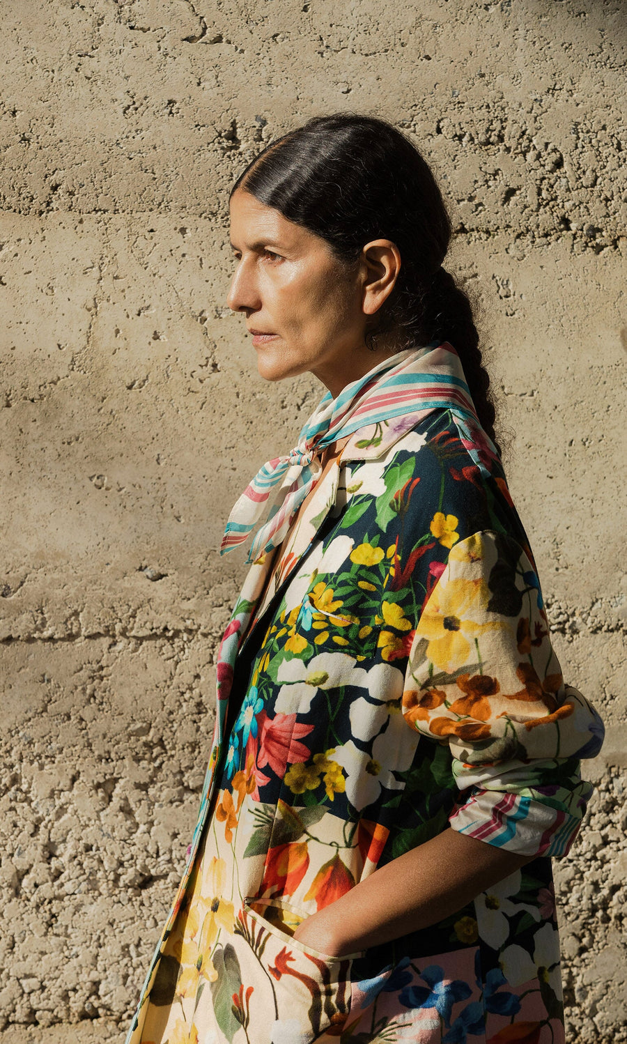 Plümo- Woman in profile wearing the Riverene Blazer, standing against a textured concrete wall.