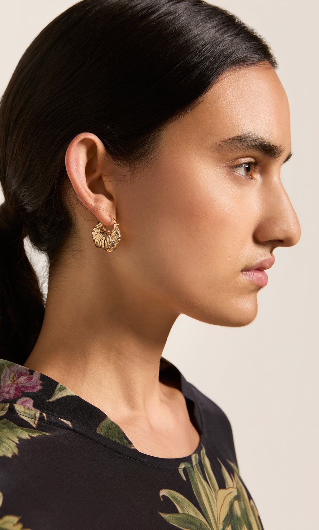 Plümo  Woman in profile with dark ponytail wears Riva Earrings and a floral-patterned top.