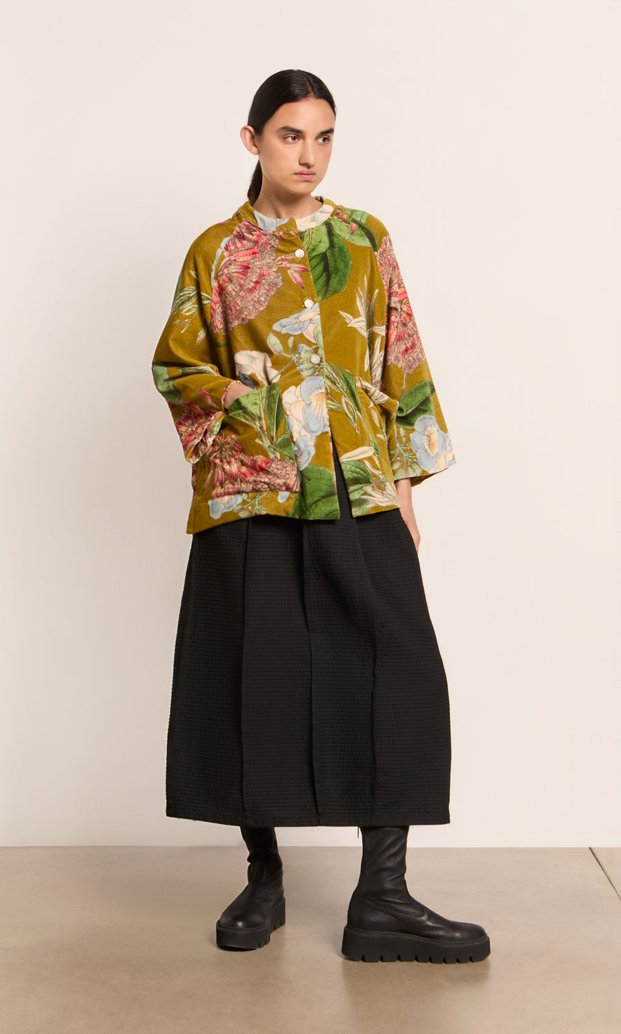 Plümo  Person in a Rodart Velvet Jacket, black culottes, and black boots stands against a plain light background.