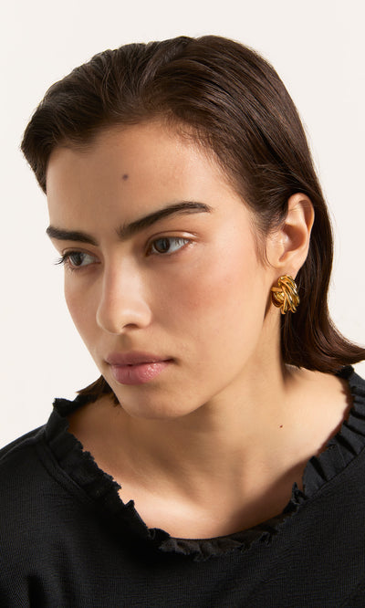 Plümo  Woman in black top and Banda Earrings, gazing sideways against a neutral background.