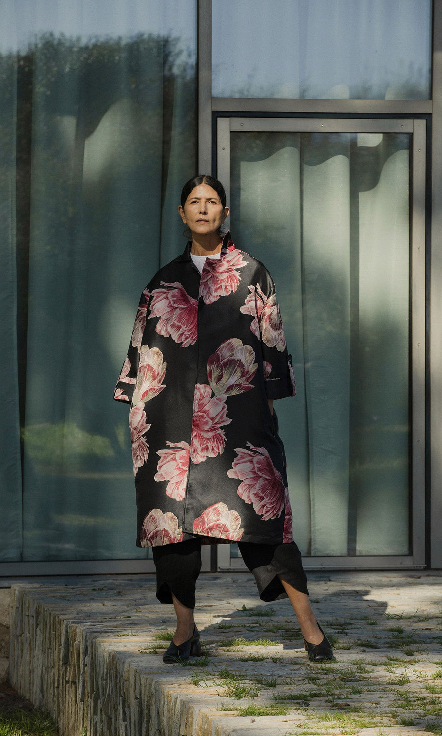 Plümo- A woman in the Rozella Coat stands outdoors before a modern glass building.