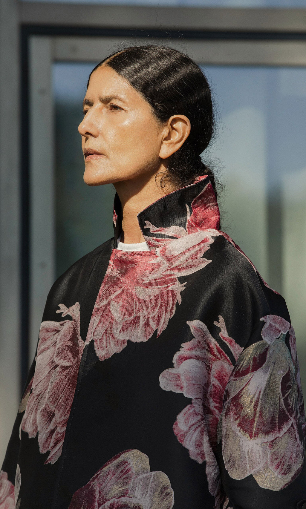 Plümo- A person with dark hair in a Rozella Coat stands in profile against a blurred background.