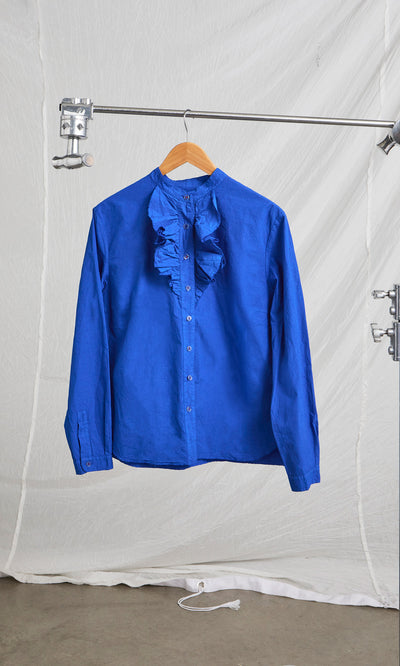 Plümo  Cobalt Ruffle Shirt with a bright blue ruffle neck hanging on a garment rack.