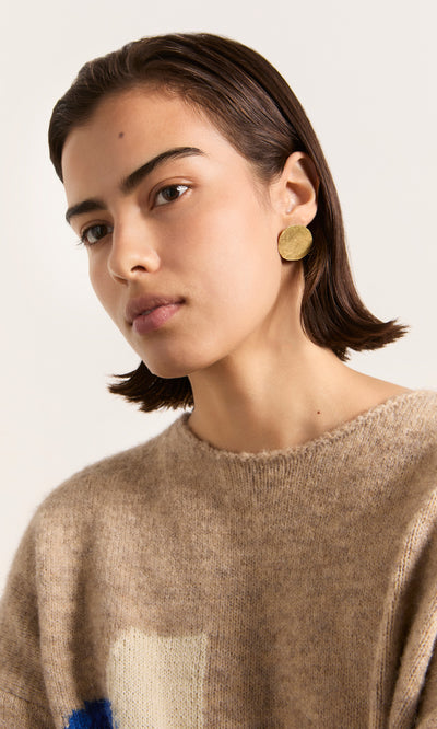 Plümo  Woman with short dark hair wears a tan sweater and Cohen Earrings, looking slightly to the side.