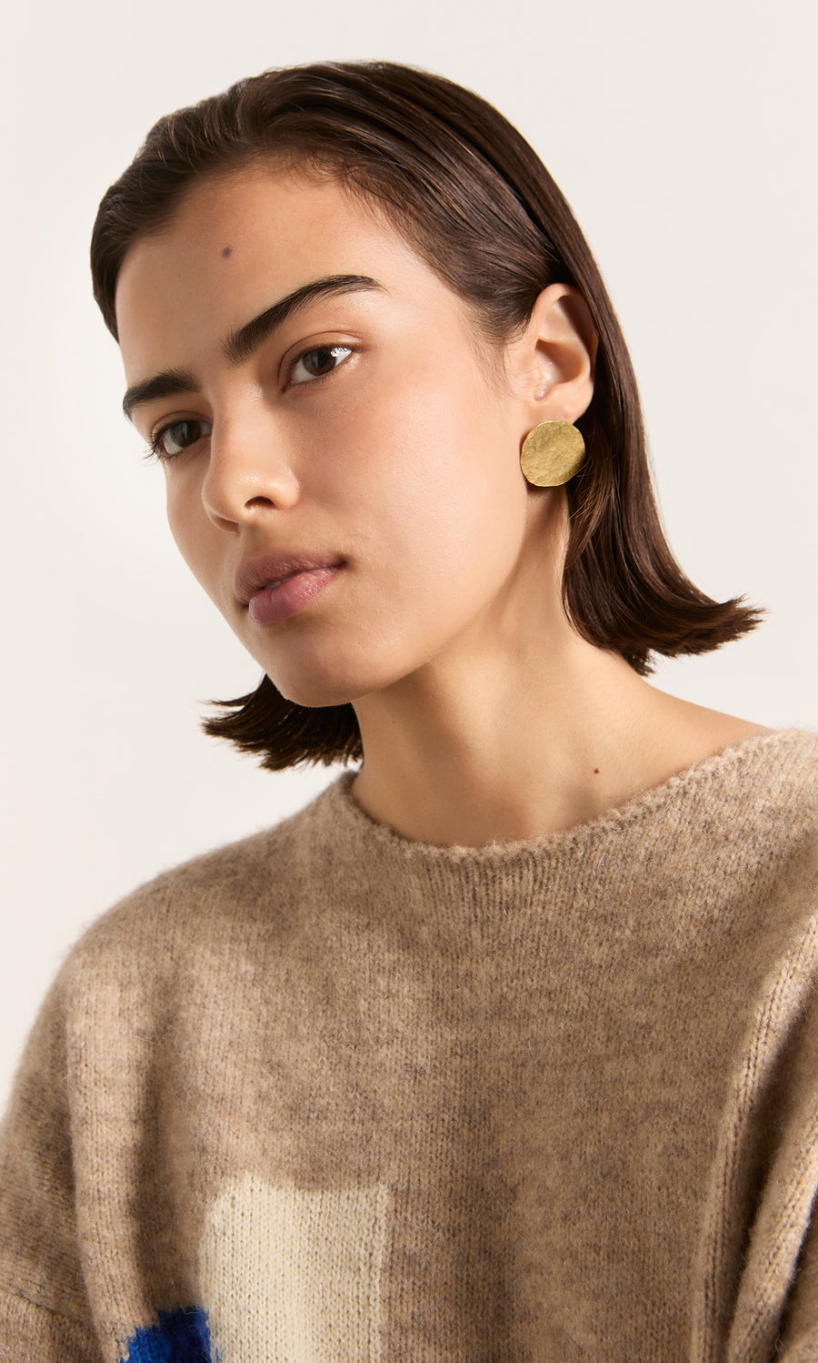 Plümo  Woman with short dark hair wears a tan sweater and Cohen Earrings, looking slightly to the side.