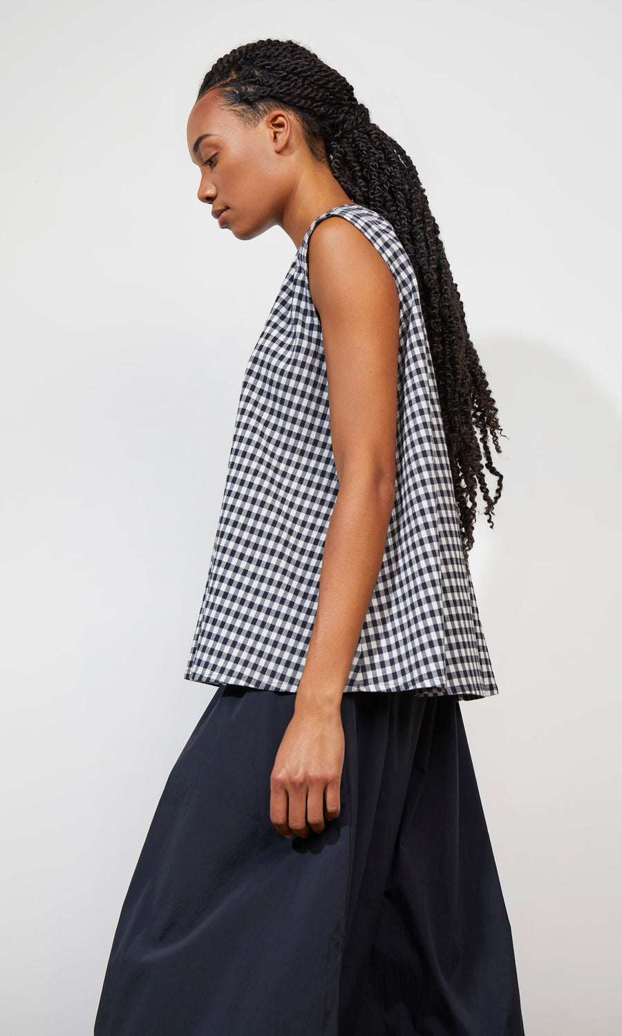 Plümo- Woman in the Serena Top - Gingham and a black skirt walking against a plain light background.