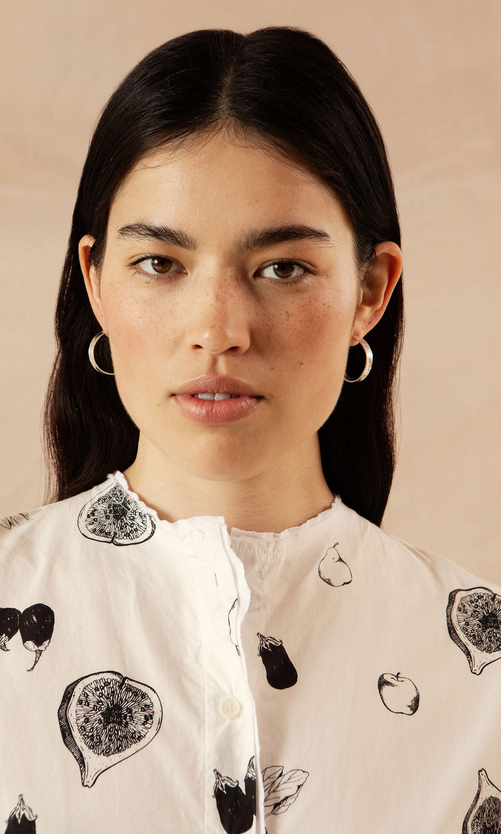 Plümo- Woman with straight dark hair wears a fruit-print top and Silver Pebble Hoops, against a neutral background.