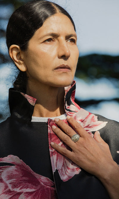 Plümo- A woman with dark hair wears a floral jacket and the Silver Wild Ring, her hand resting on her chest in sunlight.