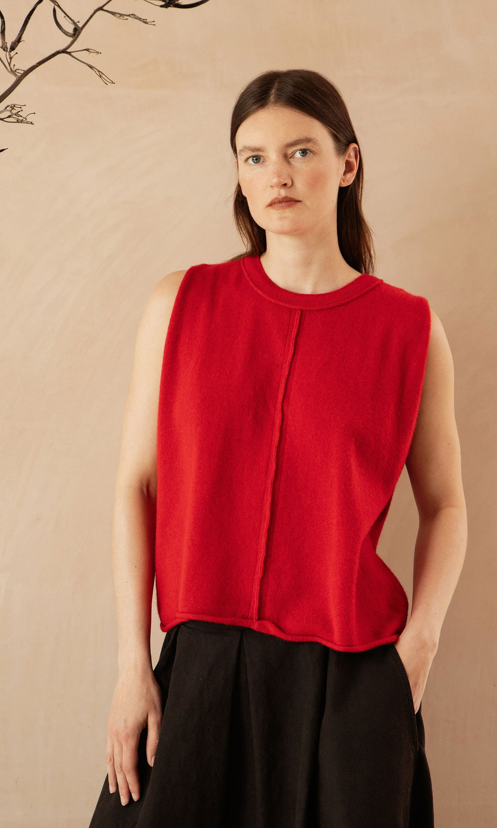 Plümo- Woman with straight brown hair wears a supersoft red Stella Tank and black skirt, standing against a beige background.