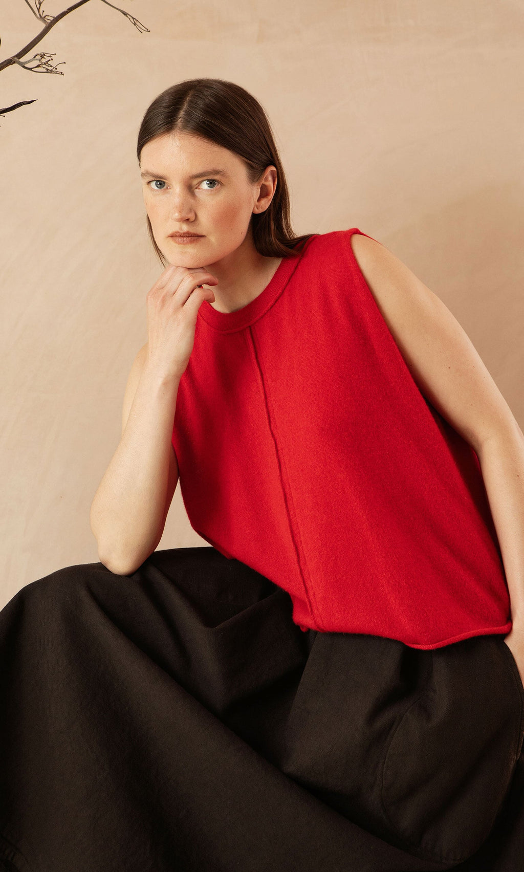 Plümo- Woman with straight brown hair wears the Stella Tank in red and a black skirt, sitting with her hand on her chin.