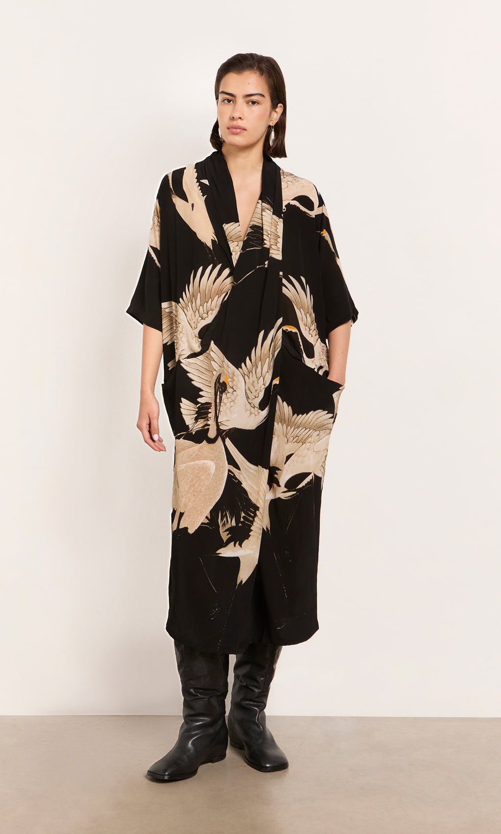 Plümo  Person wearing the Stork Twist Dress with black boots, standing against a plain white wall.