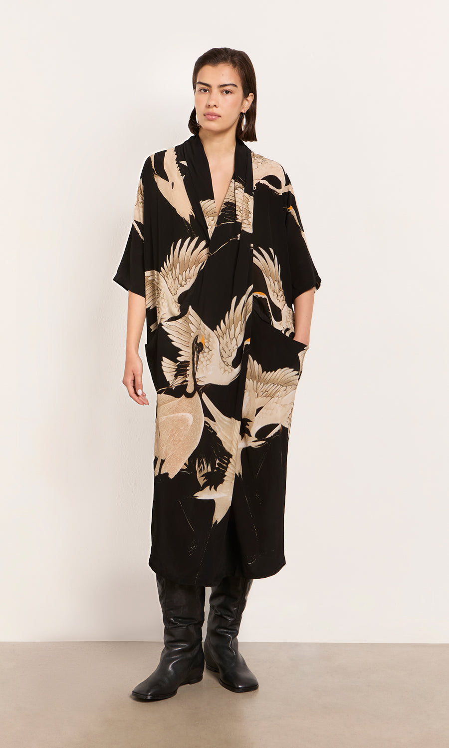 Plümo  Person wearing the Stork Twist Dress with black boots, standing against a plain white wall.