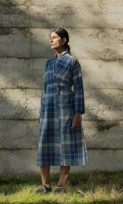 Plümo- Woman in the Wrap Tie - Check dress made from Japanese Banshu-ori stands on grass, looking to the side.