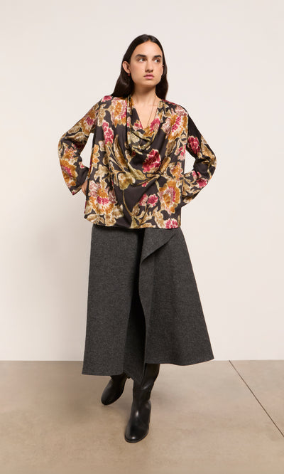 Plümo  Woman in a floral blouse, Eardley Skirt in grey wool, and black boots stands against a plain background.