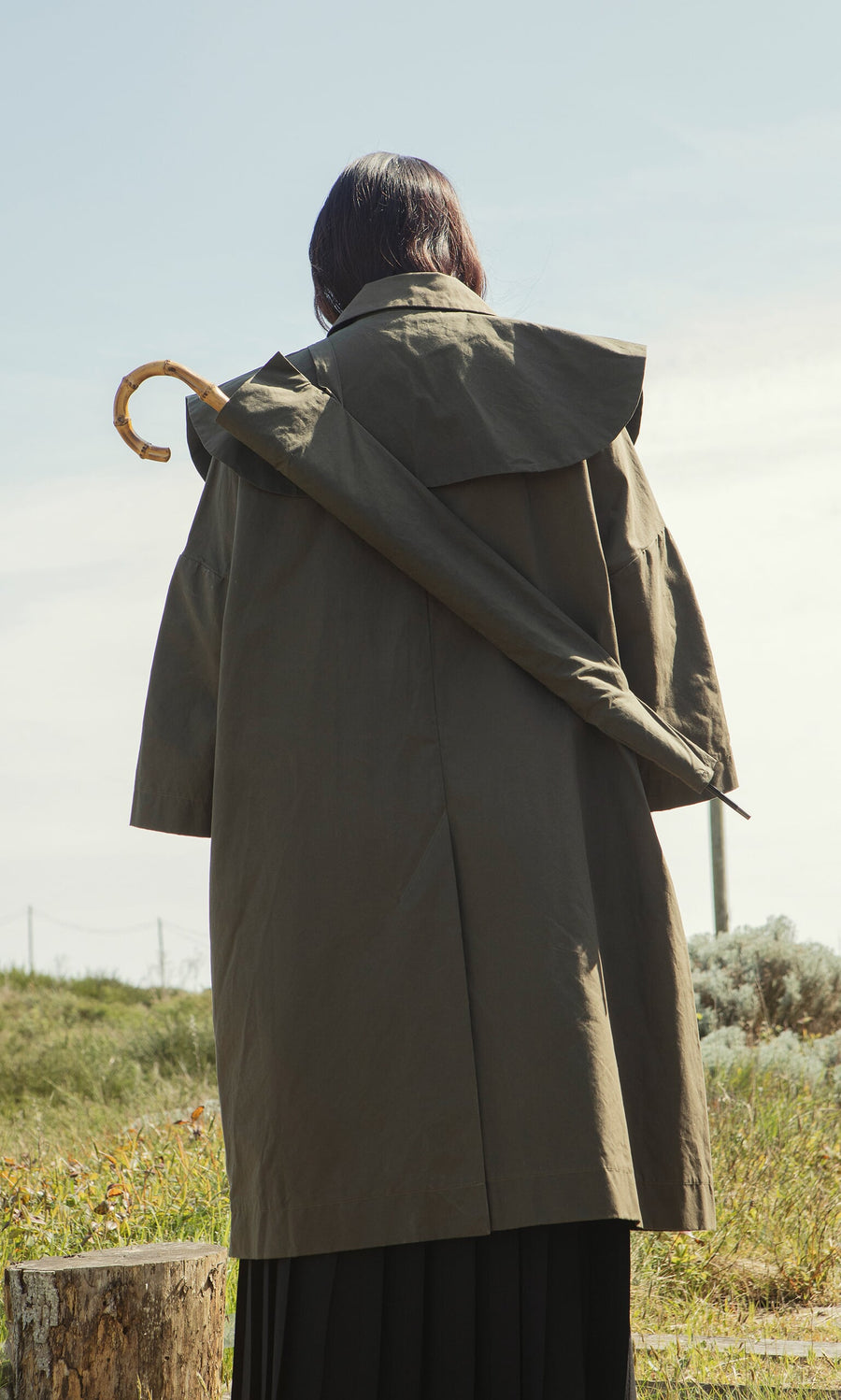 Plümo- Person stands outdoors, back to camera, carrying a Wax Umbrella Bag in olive waxed fabric over their shoulder.