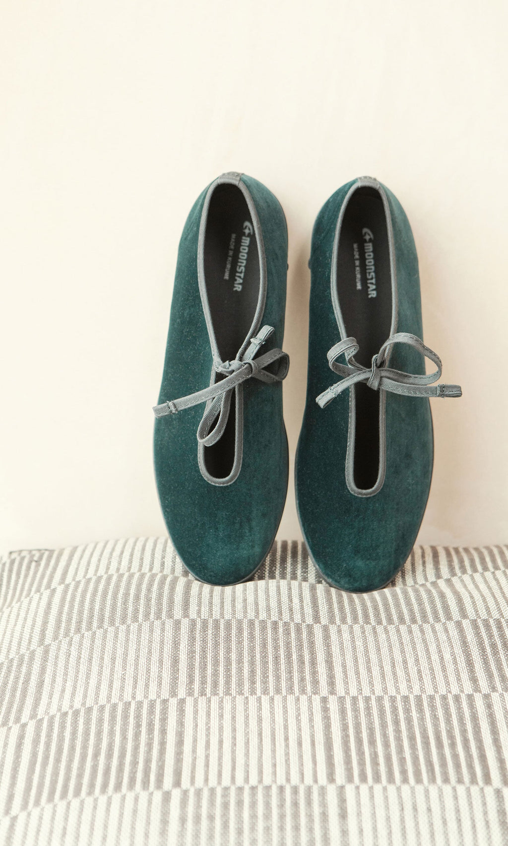 Plümo- A pair of Velvet Prim Ballerinas with bows sits neatly on a striped fabric surface.