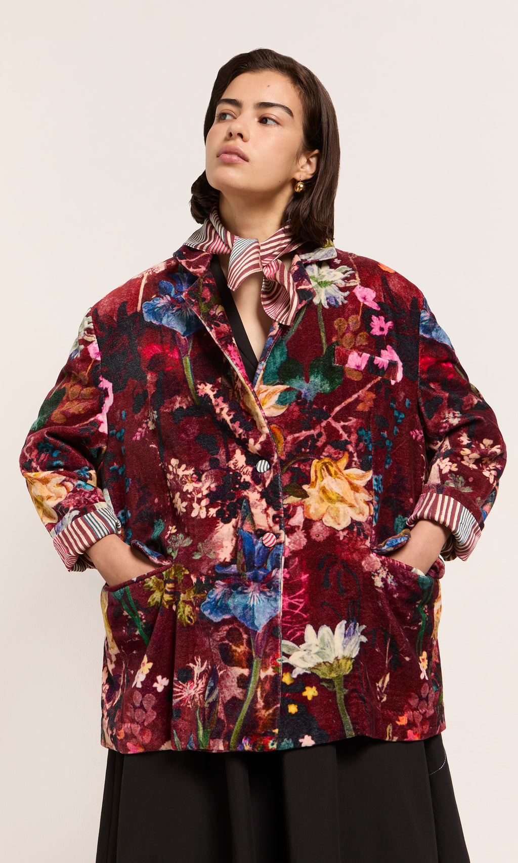 Plümo  Person in a Velvetine Blazer with Paris atelier flair, hands in pockets, striped shirt and scarf layered underneath.