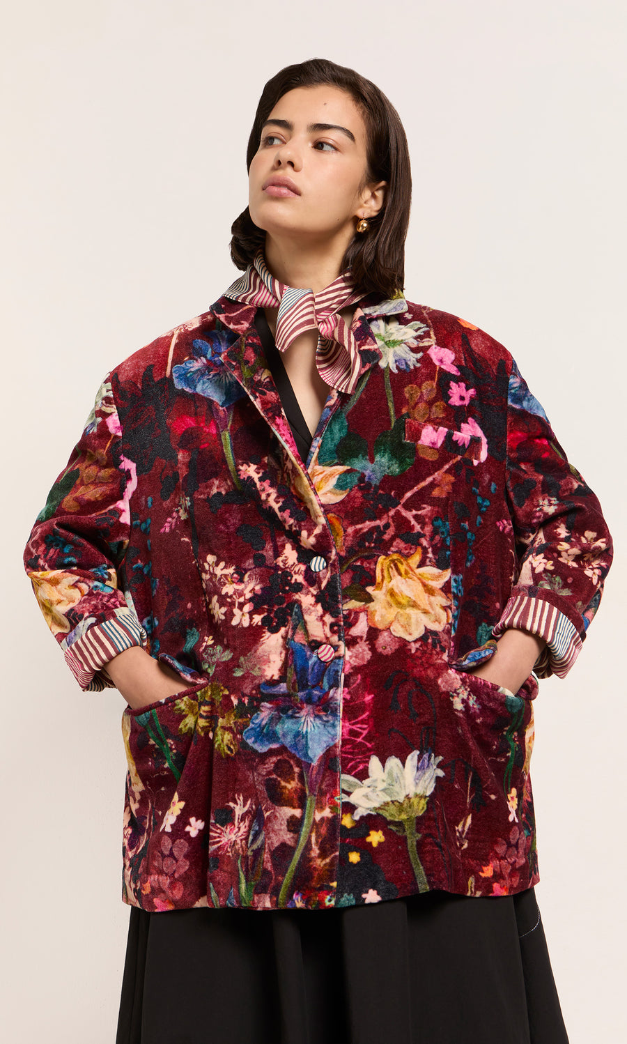 Plümo  Person in a Velvetine Blazer with Paris atelier flair, hands in pockets, striped shirt and scarf layered underneath.