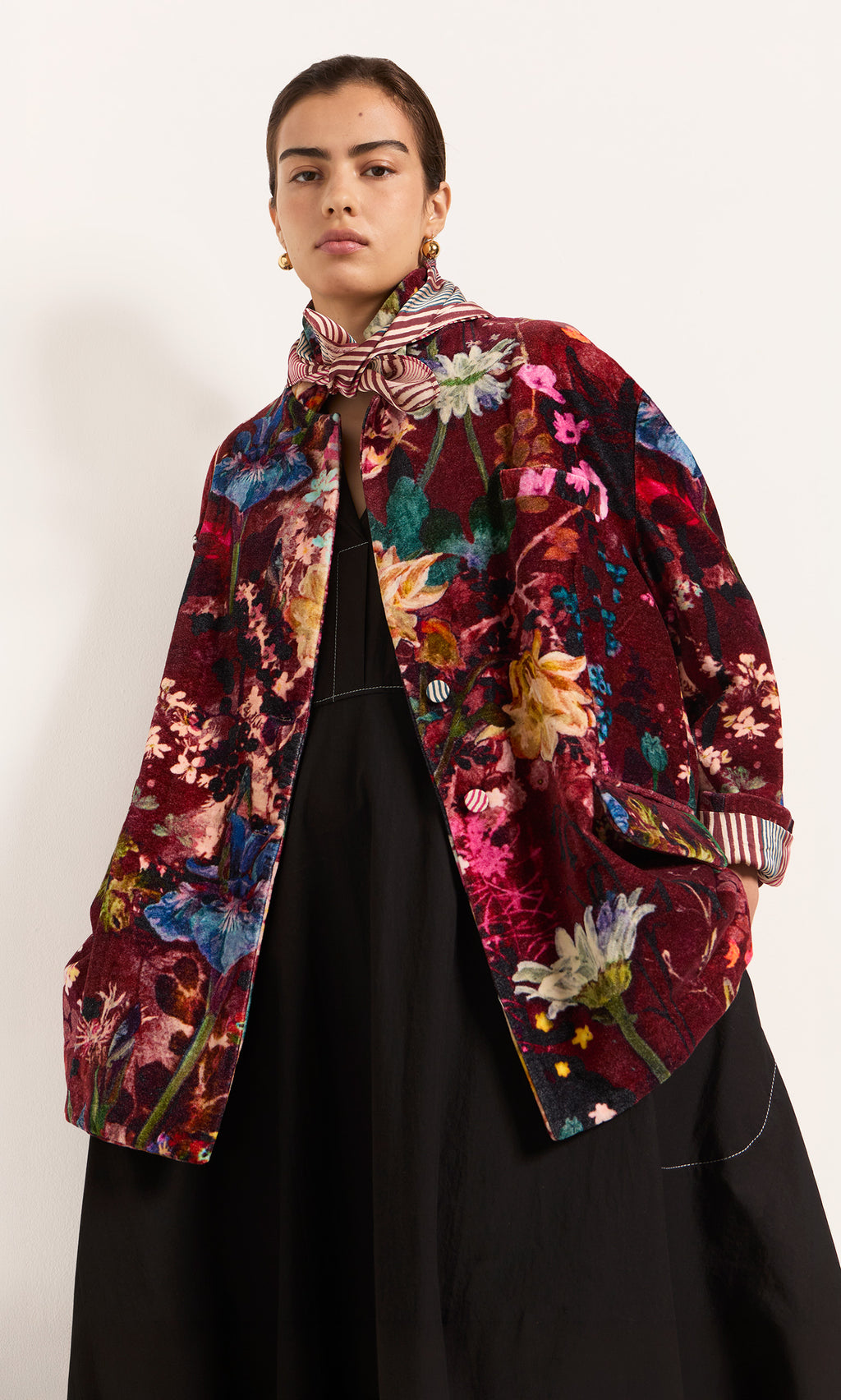 Plümo  Model wears the Velvetine Blazer with a floral design over a black dress and striped scarf, on a white background.