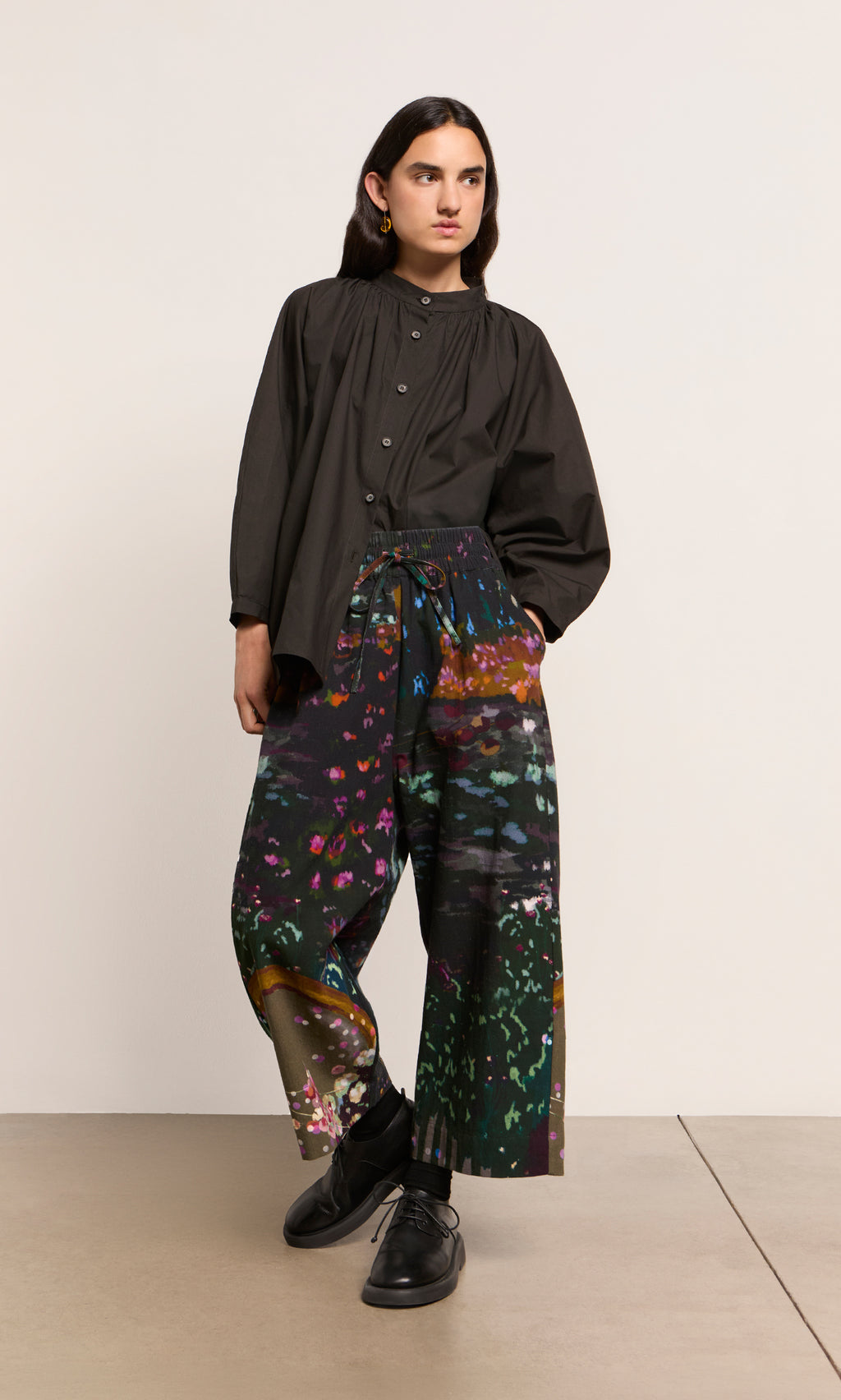 Plümo  Person in a Kroyer Blouse with balloon sleeves and vibrant floral wide-leg pants stands with one foot forward.