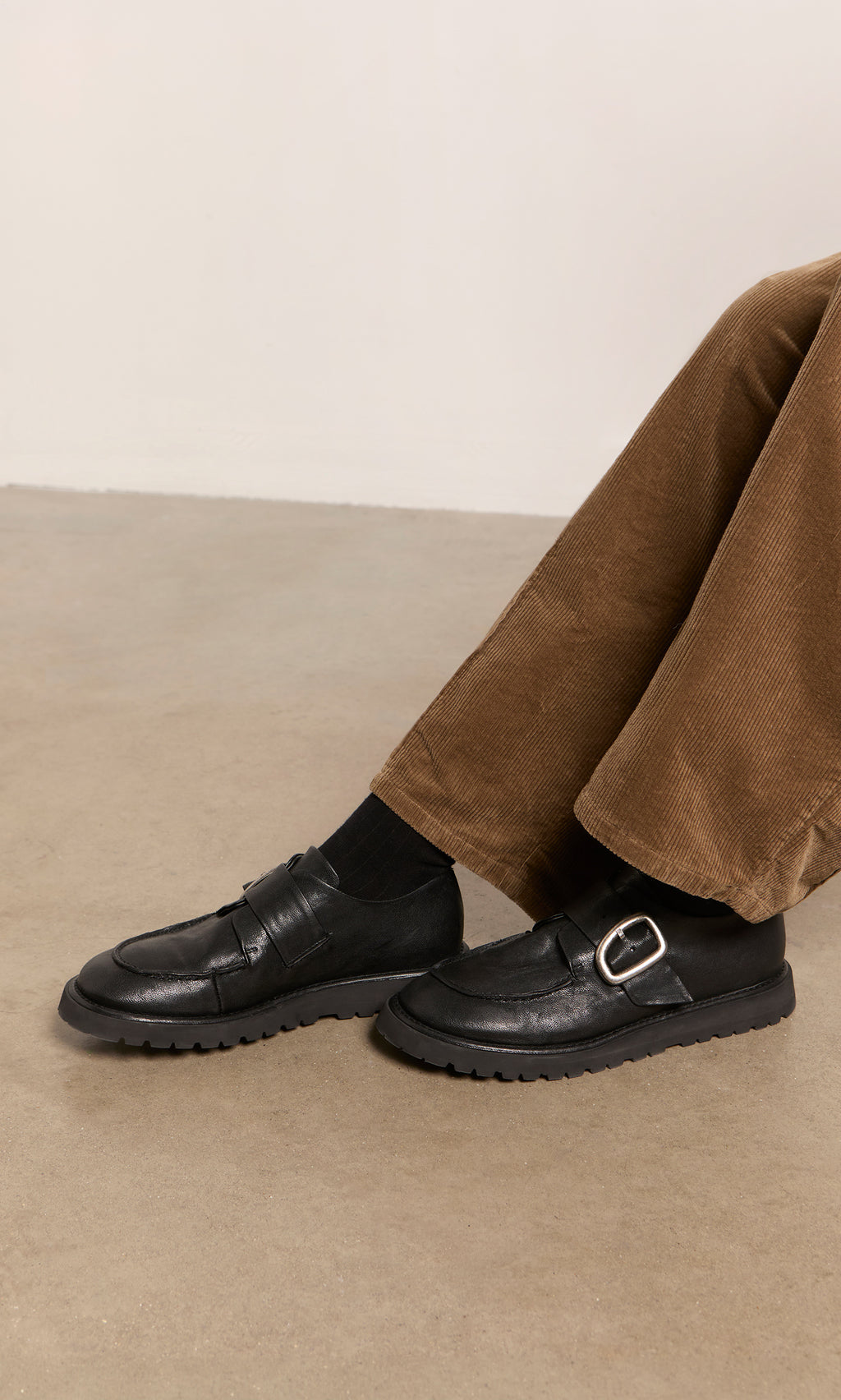 Plümo  Person in brown corduroys and Black Creepers with lugged soles, seated on a beige floor.