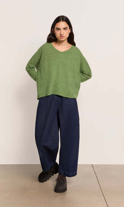 Plümo  Person in a marled green Wisher Jumper, wide navy pants, and black shoes against a plain background.