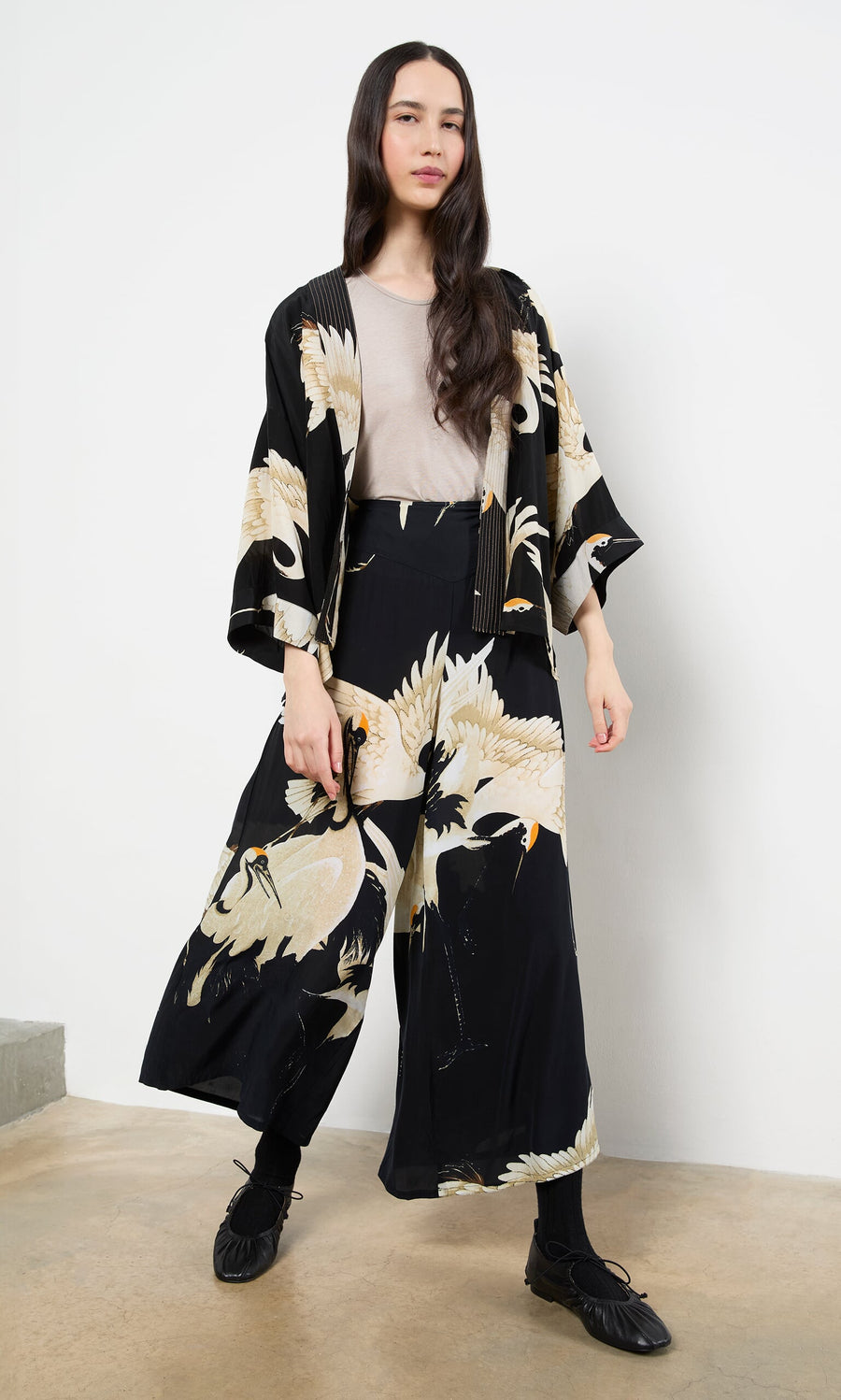 Plümo- A woman in a beige shirt and the Black Stork Kimono stands against a white wall.