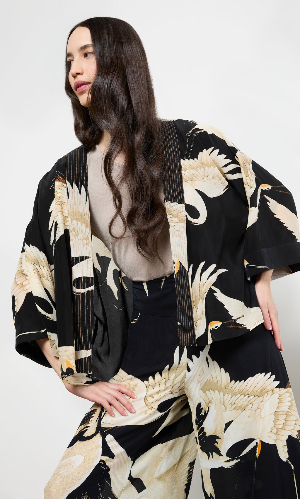 Plümo- Woman wearing the Black Stork Kimono, relaxed fit with bold stork print, posing with one hand on her hip.