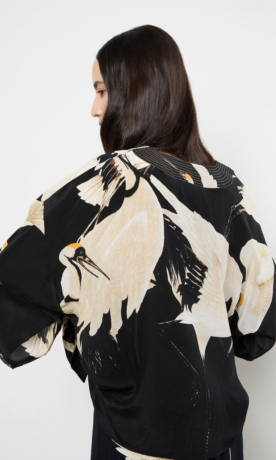 Plümo- Woman with long dark hair wears the Black Stork Kimono, a relaxed fit jacket with a large stork print on the back.