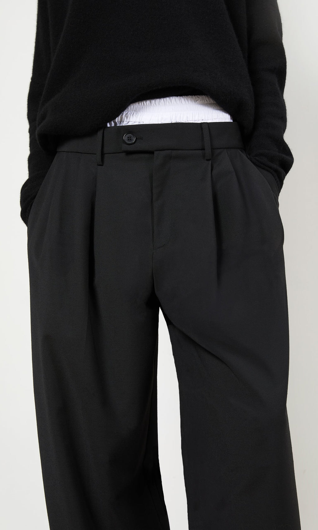 Plümo- Person wearing black Garconne Pants and a black sweater, hands in pockets, against a plain background.