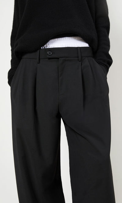 Plümo- Person wearing black Garconne Pants and a black sweater, hands in pockets, against a plain background.