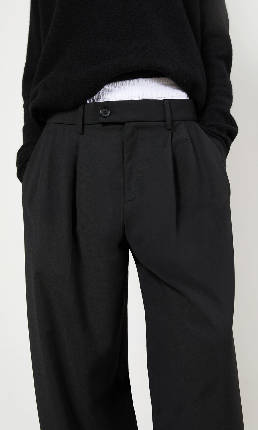 Plümo- Person wearing black Garconne Pants and a black sweater, hands in pockets, against a plain background.