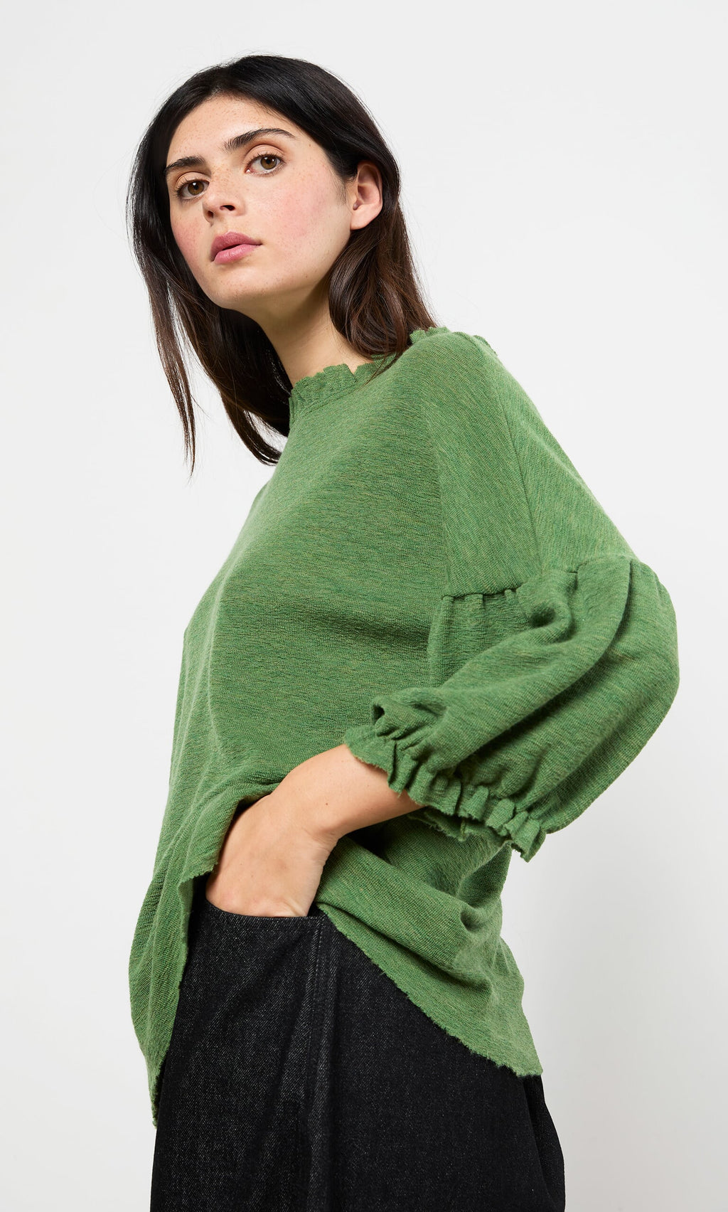 Plümo- Woman wears the Hopper Blouse, a Danish-inspired ruffle neck top, with black pants against a plain white background.