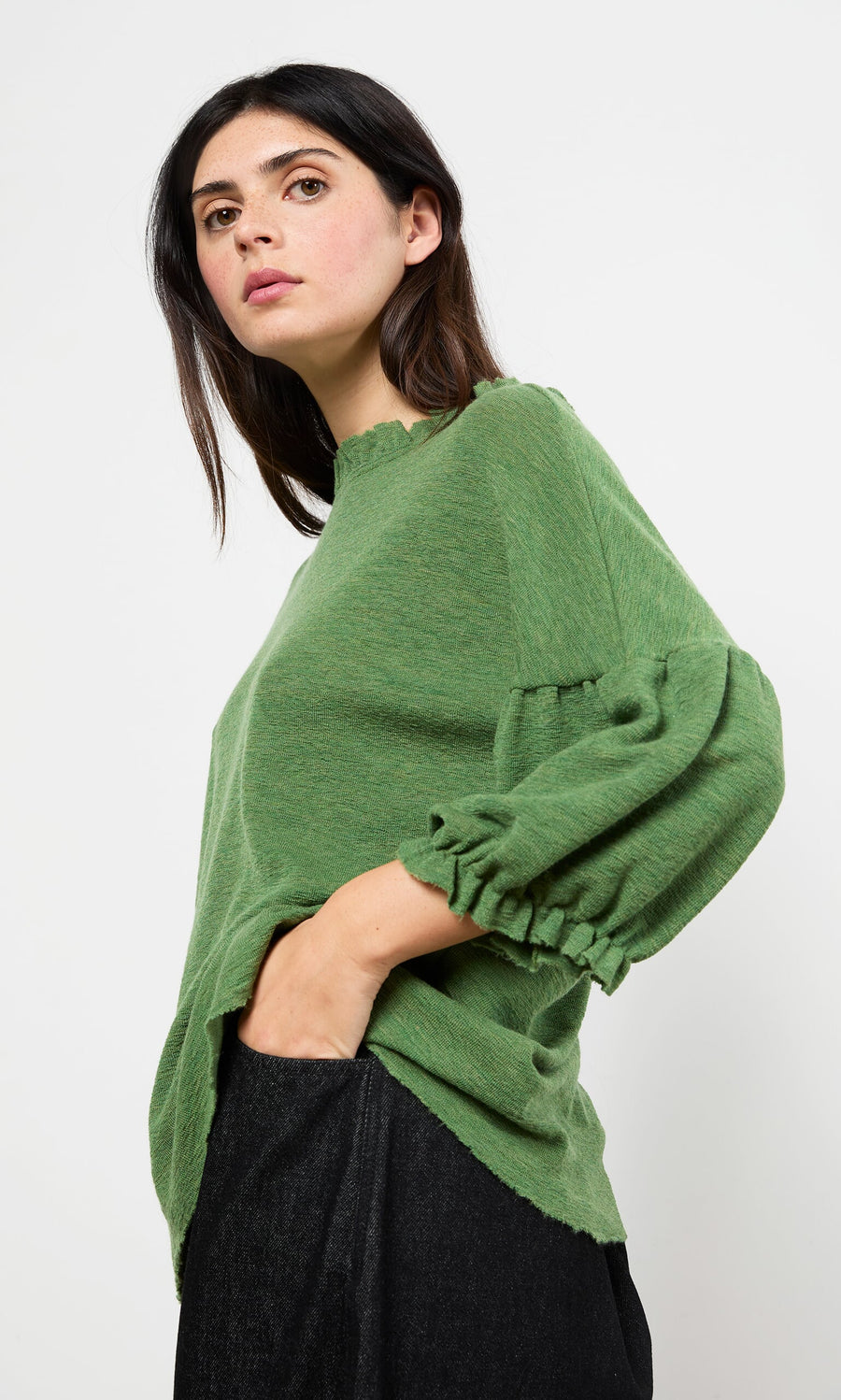 Plümo- Woman wears the Hopper Blouse, a Danish-inspired ruffle neck top, with black pants against a plain white background.