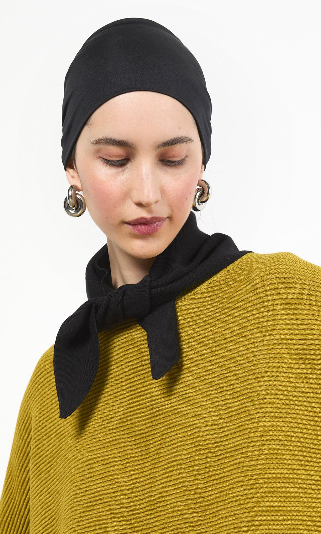 Plümo- Woman in a black headscarf, Jona Necktie - Black, gold hoop earrings, looking down with a neutral expression.