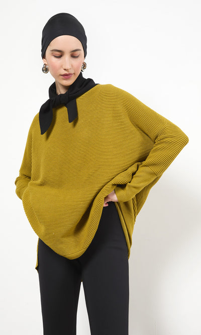Plümo- Woman in a black Jona Necktie, mustard yellow ribbed sweater, headscarf, and pants stands with one hand on her hip.