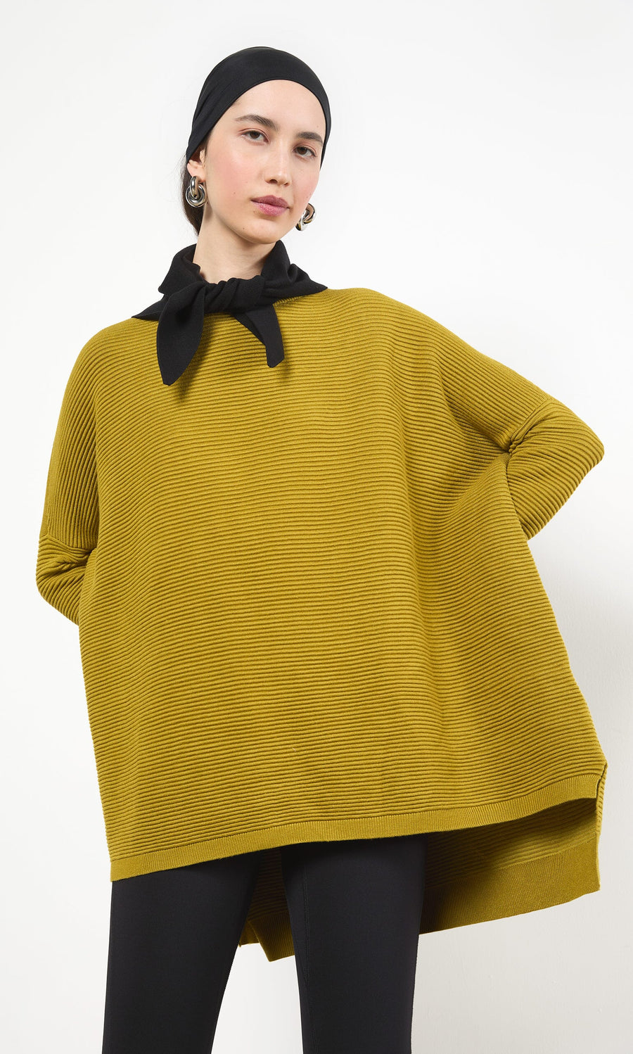 Plümo- Woman in a mustard yellow oversized top, Jona Necktie - Black, earrings, and black pants on a white background.