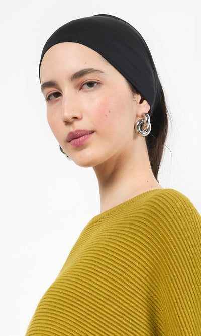 Plümo- Woman wearing a Black Wide Headband and silver hoop earrings with a mustard yellow ribbed top, looking at the camera.