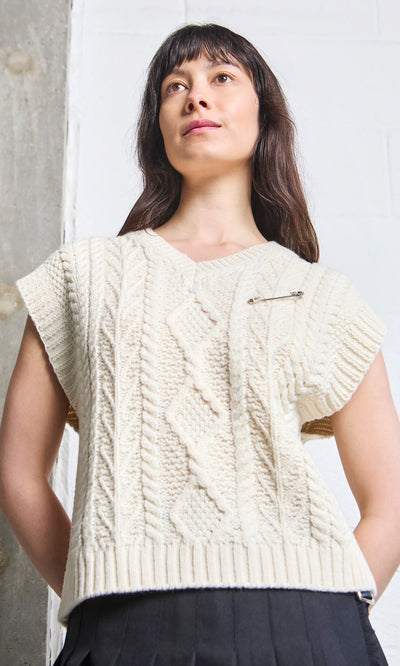 Plümo A woman styles a cream cable knit sleeveless sweater with a Kilt Pin, standing by a concrete and white wall.