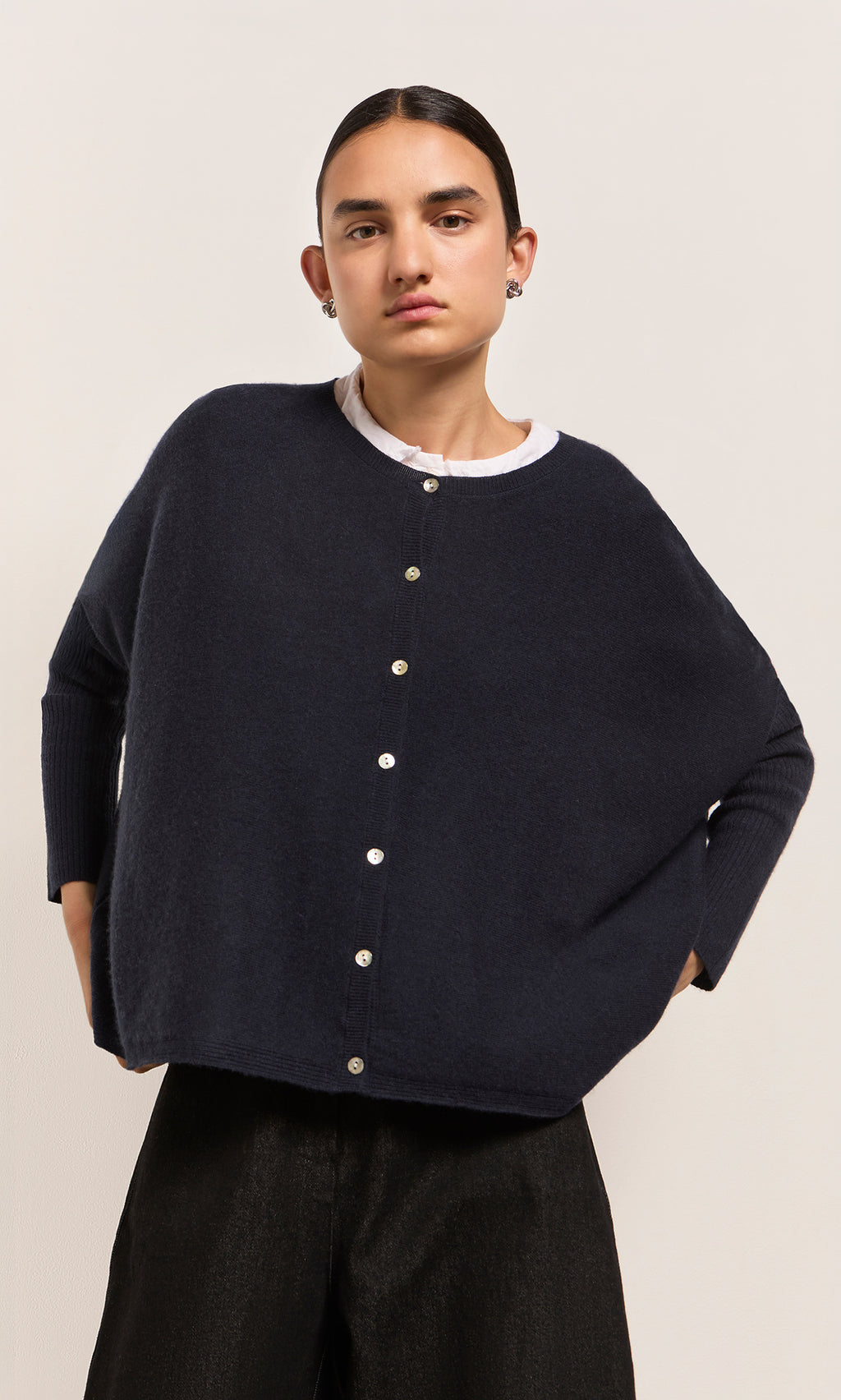 Plümo  Model in Alma Cardigan - Dark Navy over a white shirt, standing against a plain, light-colored background.