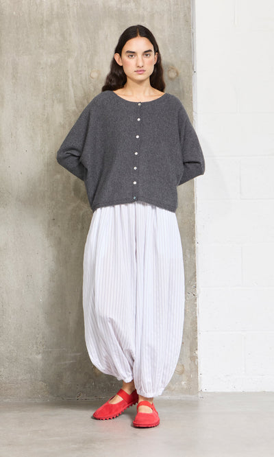 Plümo- A woman in a gray sweater and Vento Pants with an elasticated waist stands against a concrete and white wall.