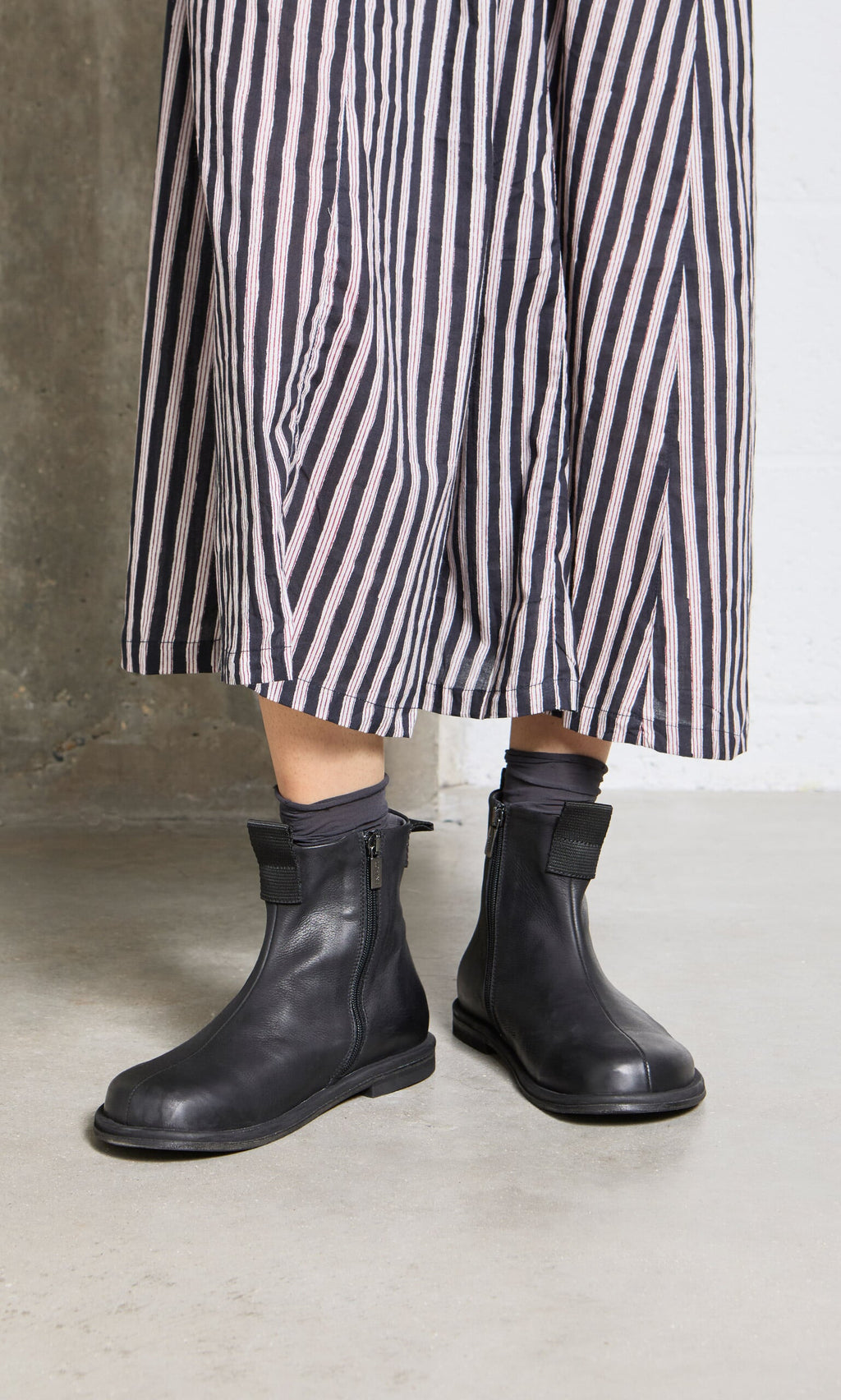 Plümo- Person wearing a long, striped skirt and Ancona Boots, standing on a concrete floor.